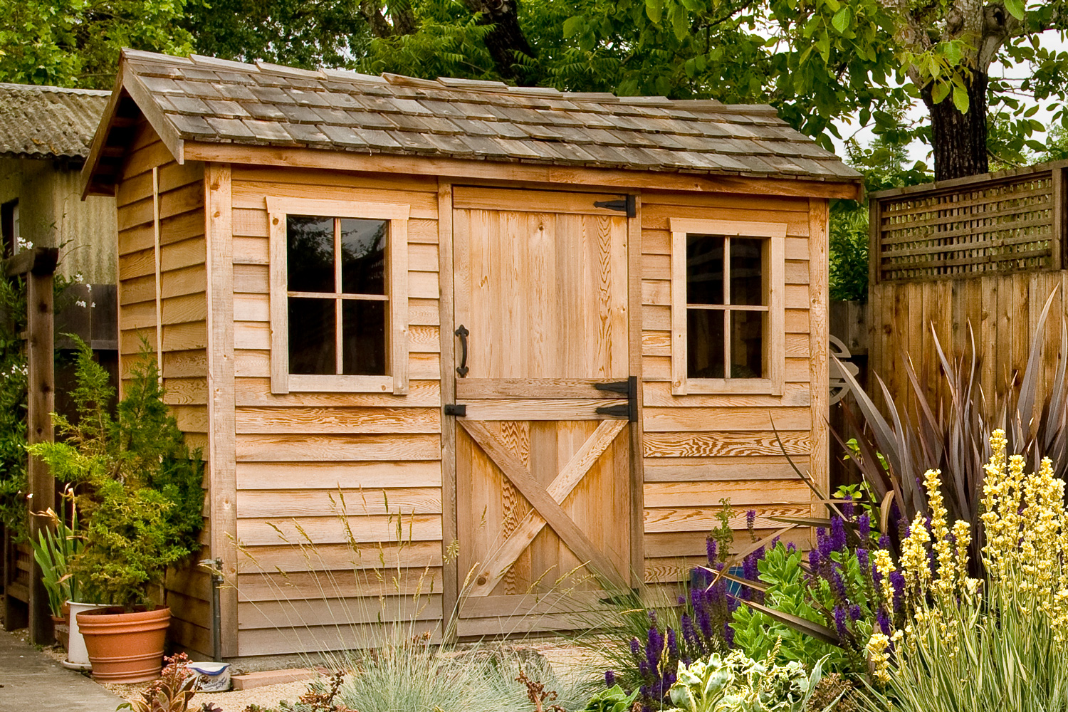 Wooden garden shed in a garden with flowers.